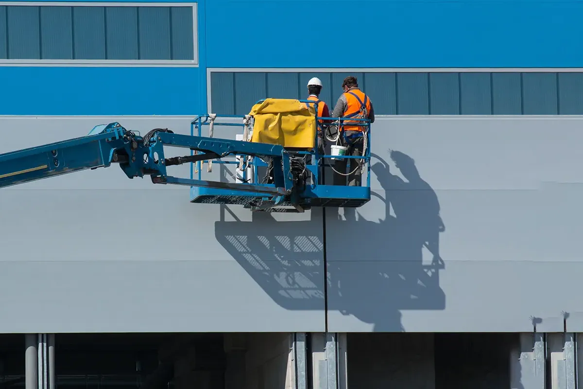 Two men working in a boom lift bucket on side of building